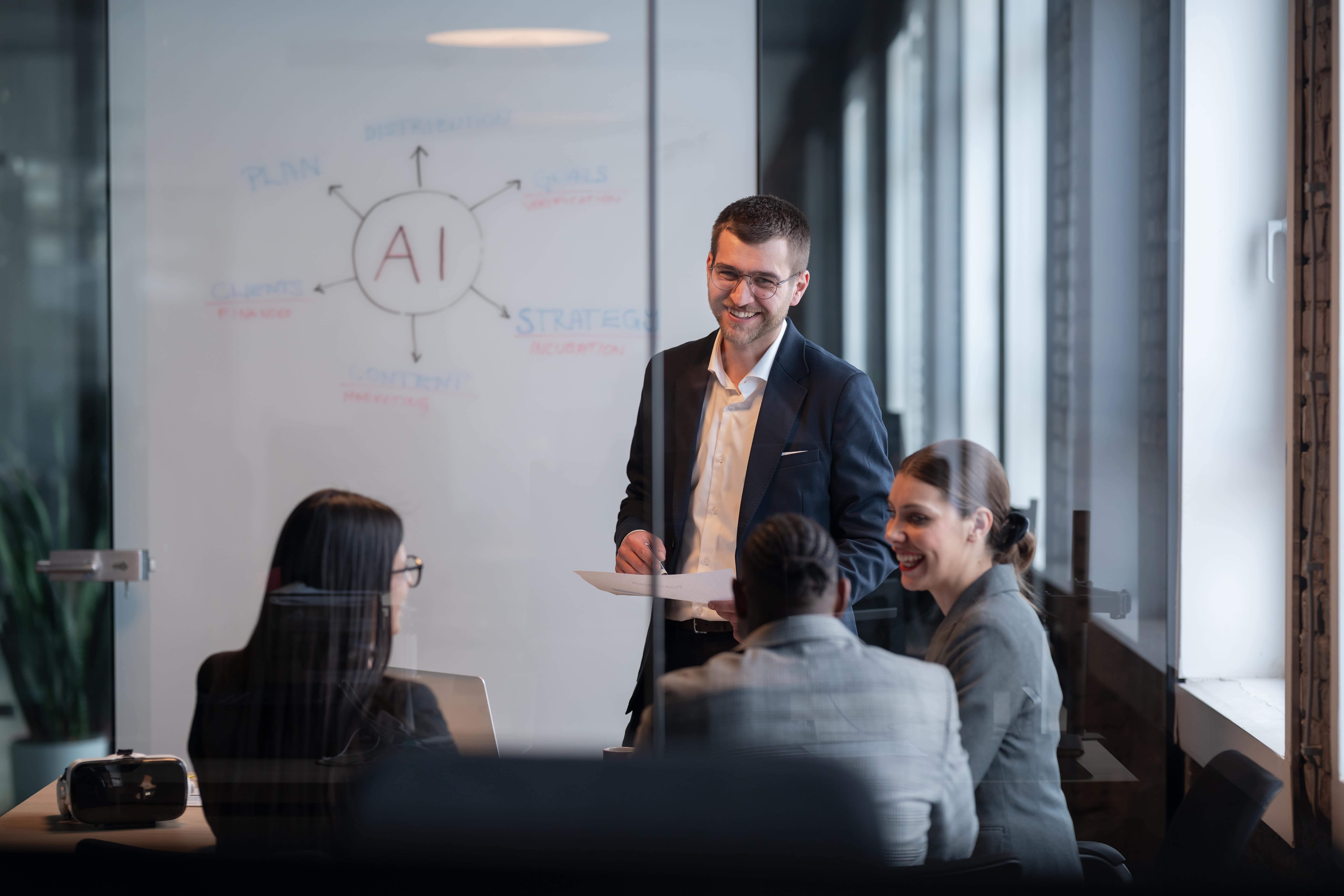 man with glasses talking in front of a whiteboard about AI